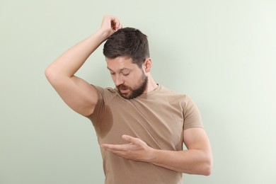 Emotional man in t-shirt before using deodorant on light green background