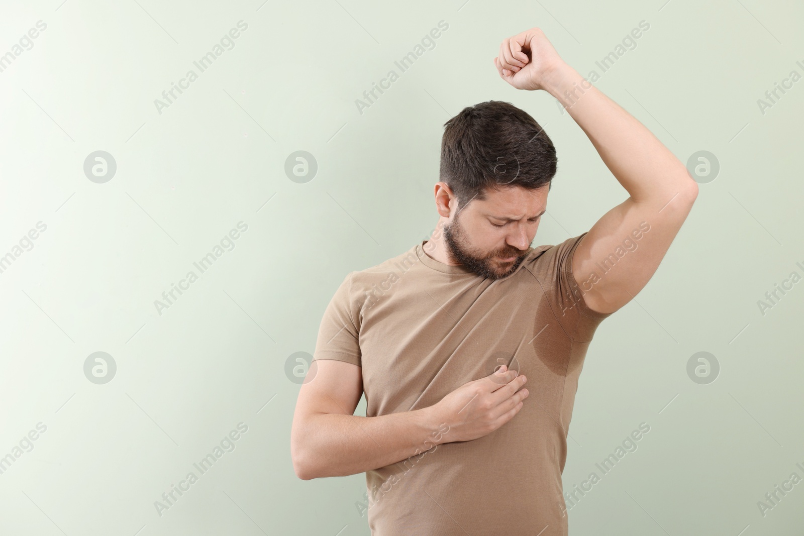 Photo of Emotional man in t-shirt before using deodorant on light green background. Space for text