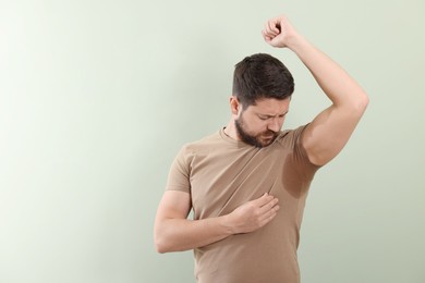 Emotional man in t-shirt before using deodorant on light green background. Space for text