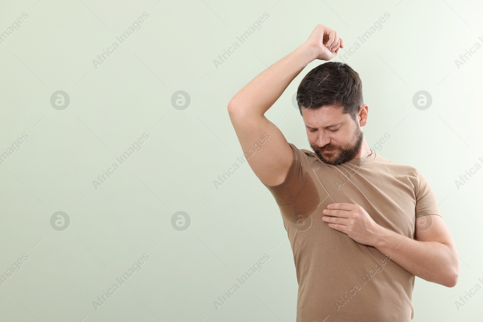 Photo of Emotional man in t-shirt before using deodorant on light green background. Space for text