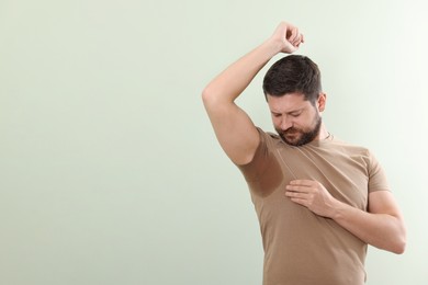 Emotional man in t-shirt before using deodorant on light green background. Space for text