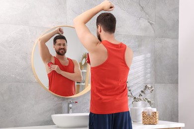 Smiling man applying solid deodorant near mirror at home