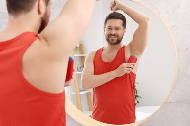 Photo of Smiling man applying solid deodorant near mirror at home