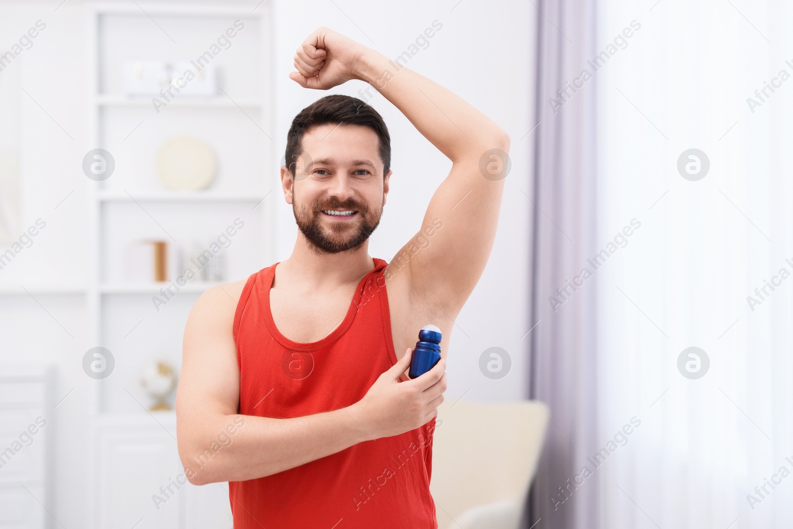 Photo of Smiling man applying roll-on deodorant at home