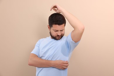 Emotional man in t-shirt before using deodorant on beige background