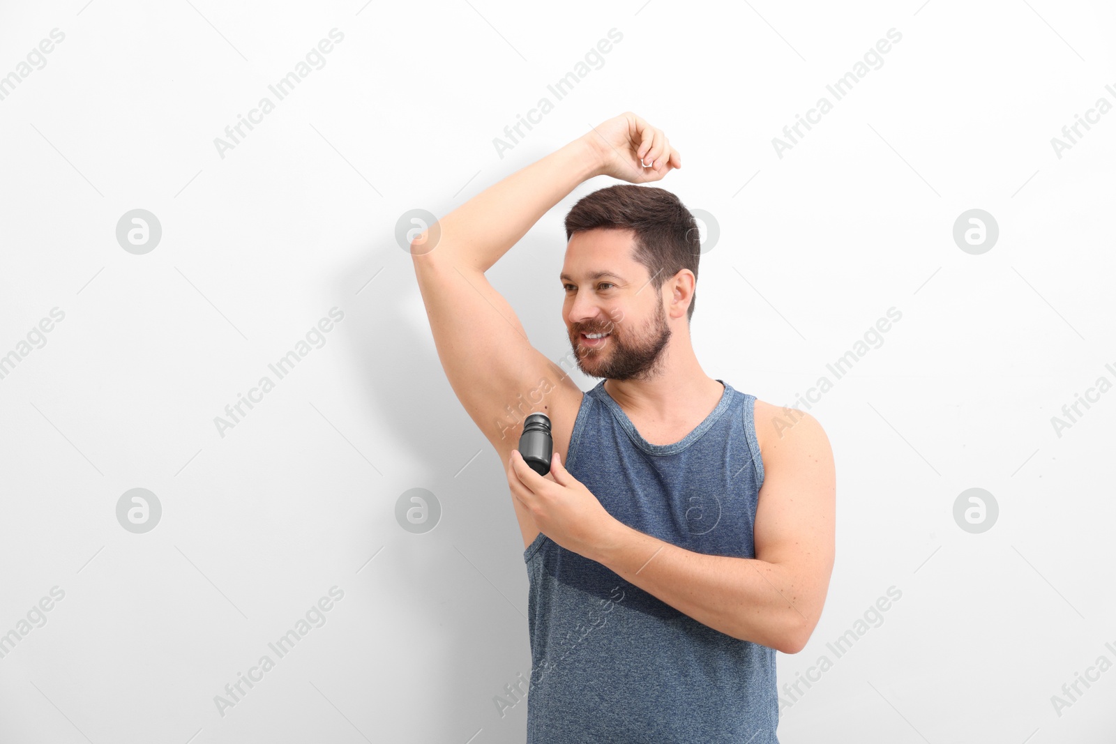 Photo of Smiling man applying roll-on deodorant on white background. Space for text