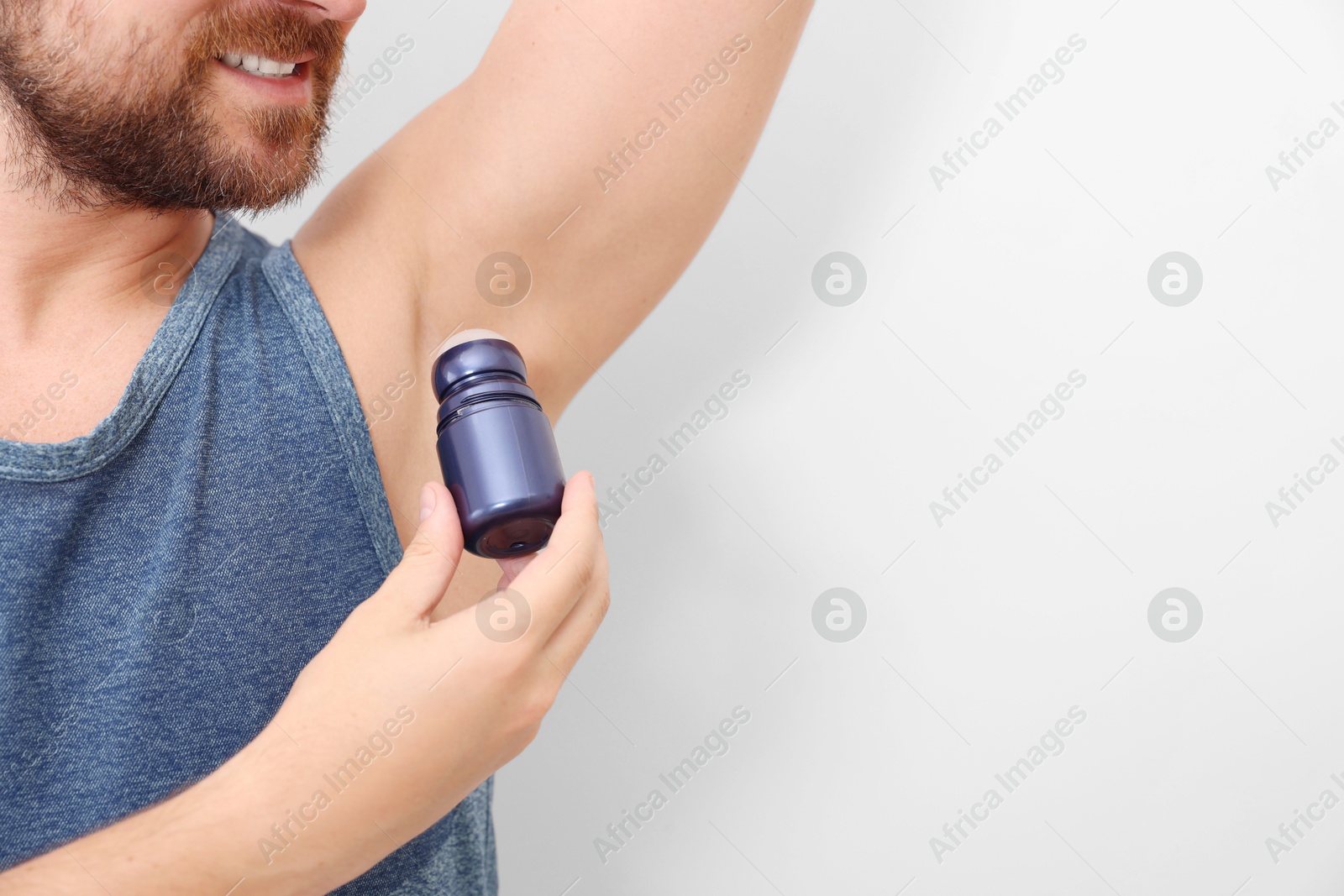 Photo of Smiling man applying roll-on deodorant on white background, closeup. Space for text