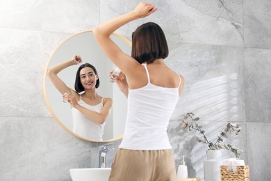 Photo of Smiling woman applying roll-on deodorant near mirror at home, back view