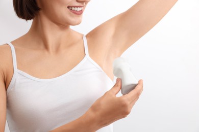 Smiling woman applying roll-on deodorant on white background, closeup