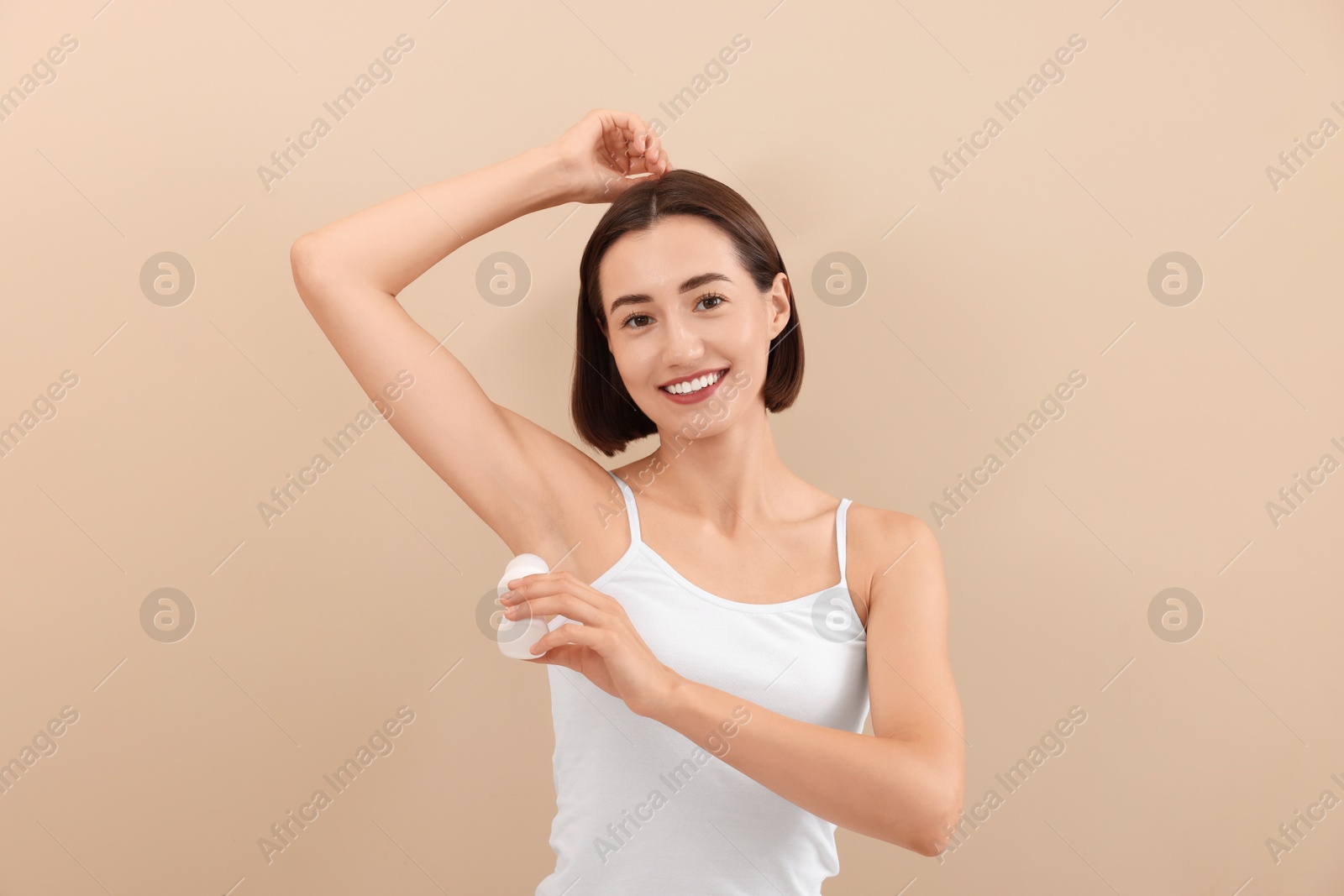 Photo of Smiling woman applying roll-on deodorant on beige background