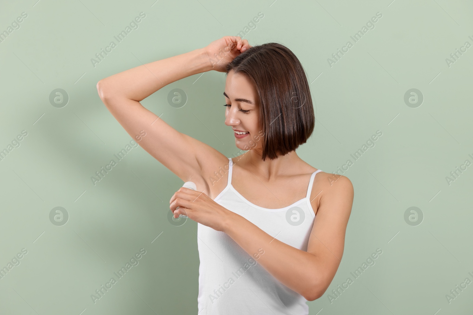 Photo of Smiling woman applying roll-on deodorant on green background