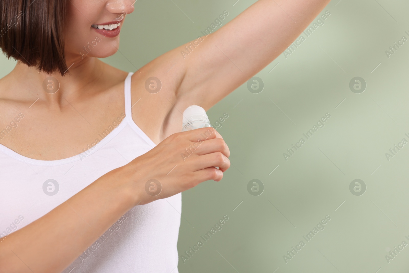 Photo of Smiling woman applying roll-on deodorant on green background, closeup. Space for text