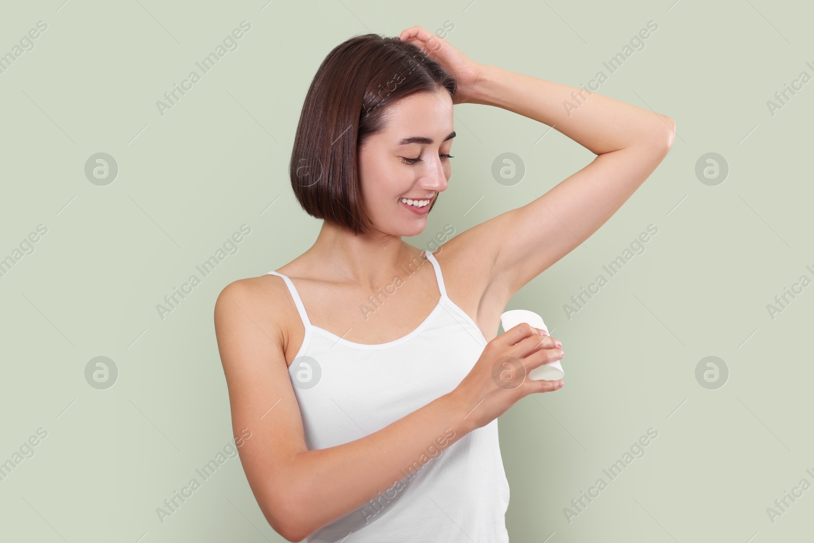 Photo of Smiling woman applying solid deodorant on green background