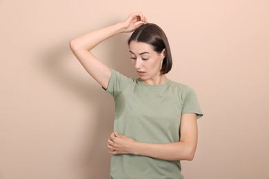 Emotional woman in t-shirt before using deodorant on beige background