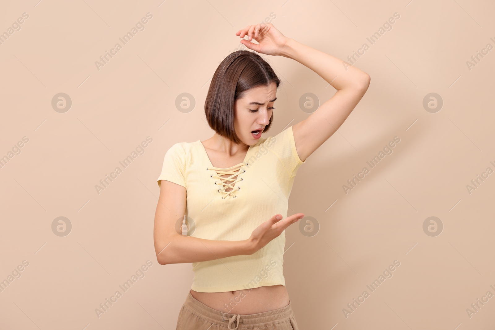 Photo of Emotional woman in t-shirt before using deodorant on beige background