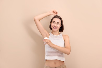 Photo of Smiling woman applying solid deodorant on beige background