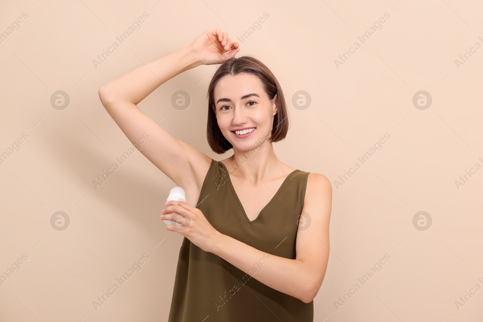 Photo of Smiling woman applying roll-on deodorant on beige background