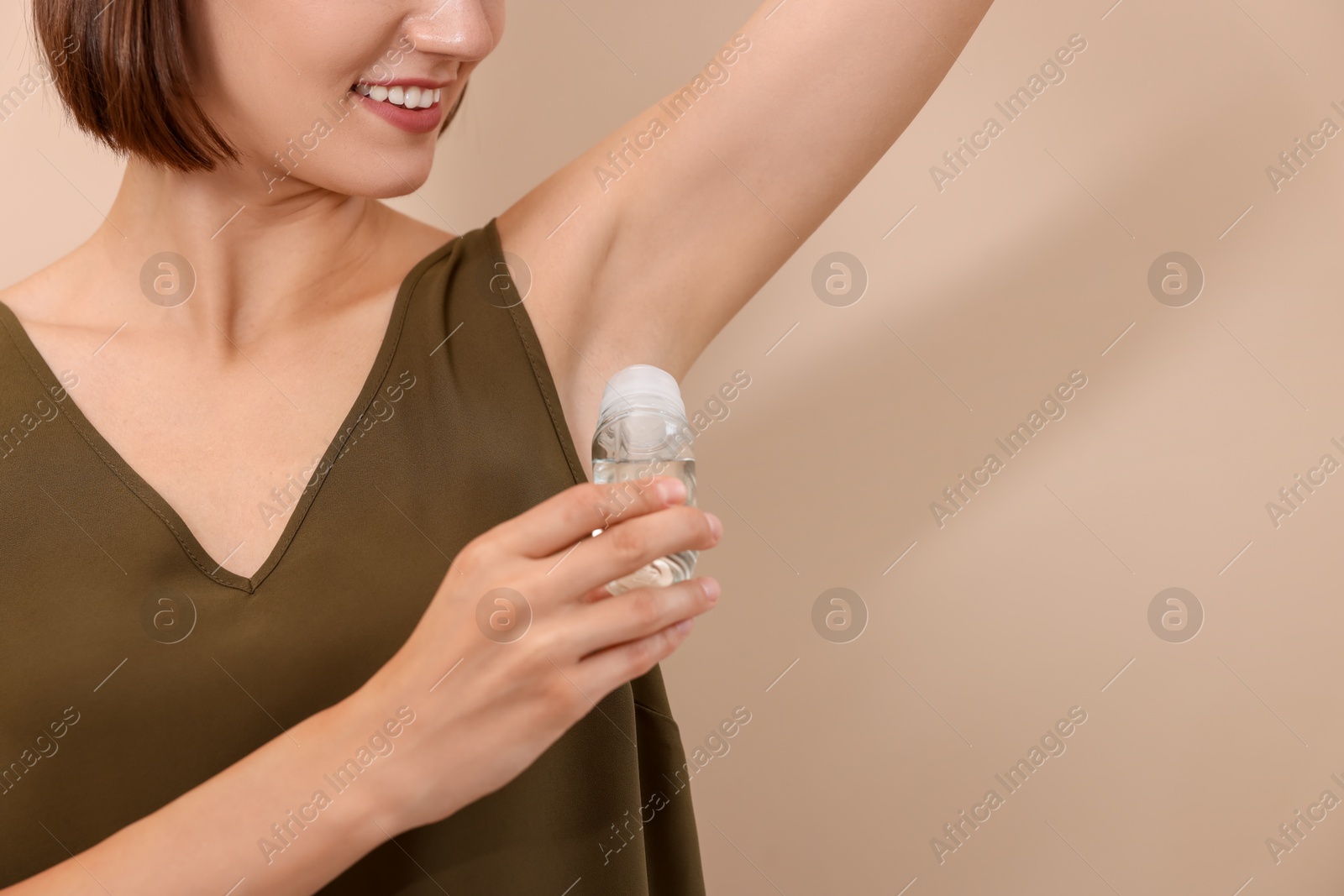 Photo of Smiling woman applying roll-on deodorant on beige background, closeup. Space for text