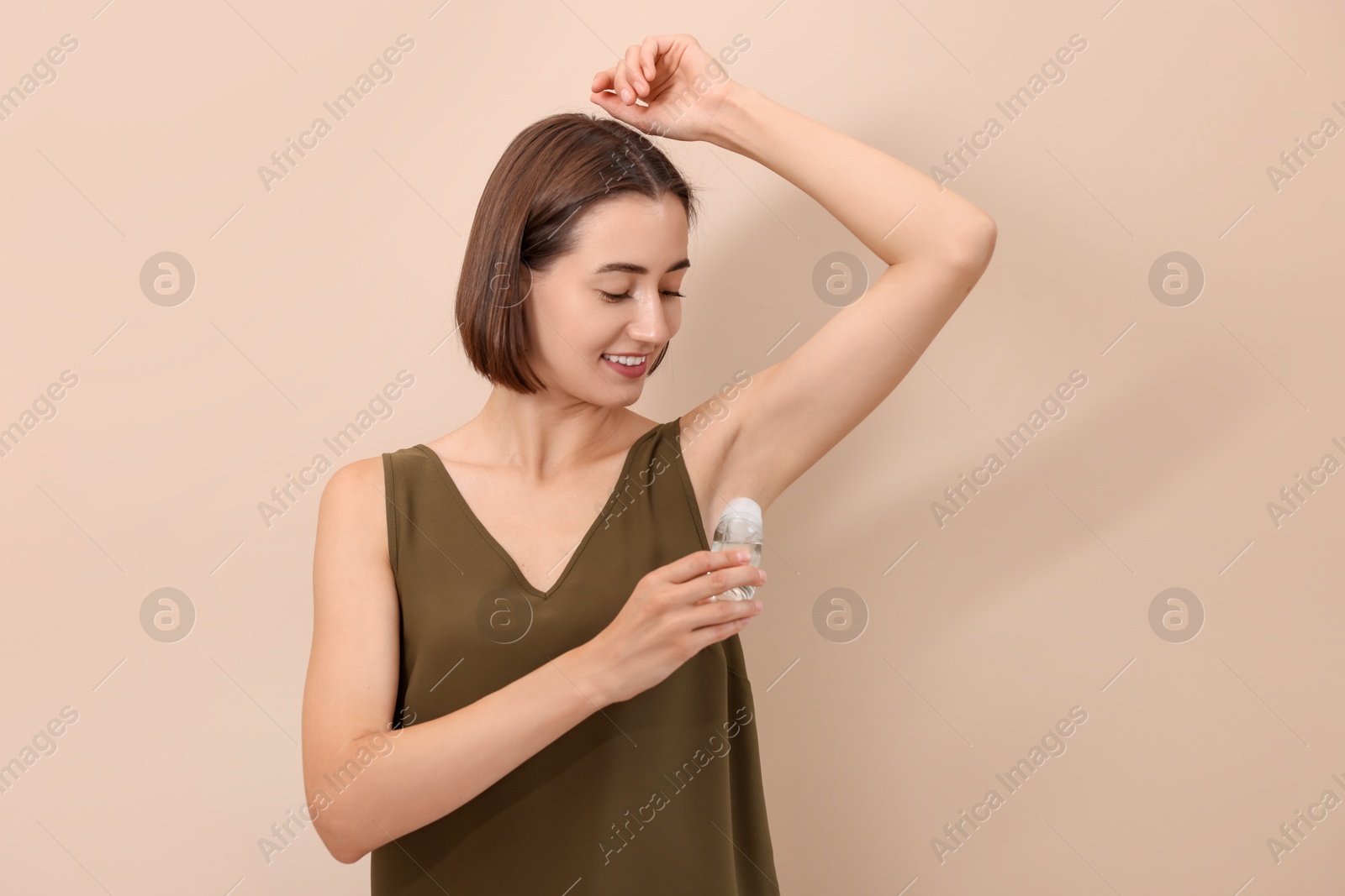 Photo of Smiling woman applying roll-on deodorant on beige background