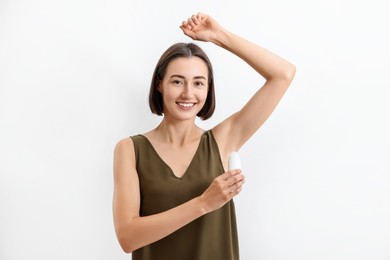 Smiling woman applying roll-on deodorant on white background