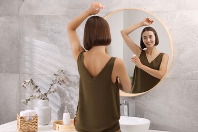 Photo of Smiling woman applying roll-on deodorant near mirror at home, back view