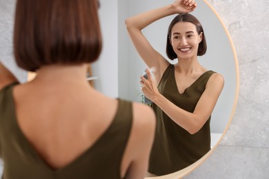 Photo of Smiling woman applying spray deodorant near mirror at home, back view