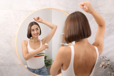 Photo of Smiling woman applying roll-on deodorant near mirror at home, back view