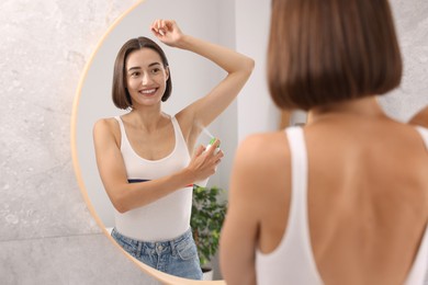 Photo of Smiling woman applying spray deodorant near mirror at home, back view