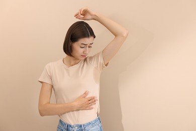 Emotional woman in t-shirt before using deodorant on beige background. Space for text