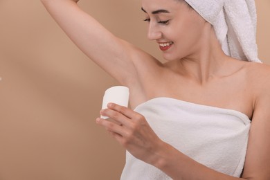 Smiling woman applying solid deodorant on beige background