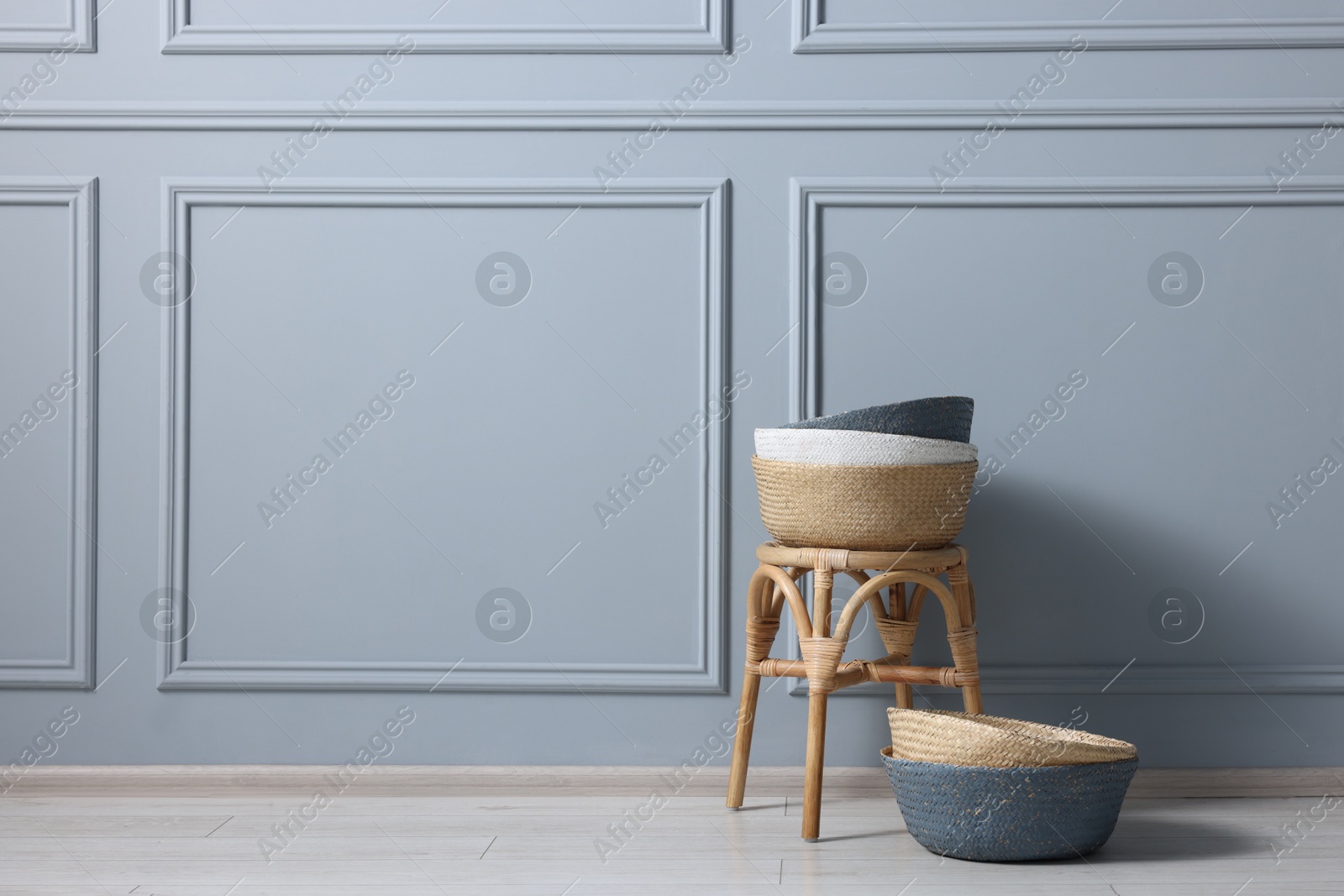 Photo of Stylish stool and many wicker baskets near light grey wall indoors, space for text