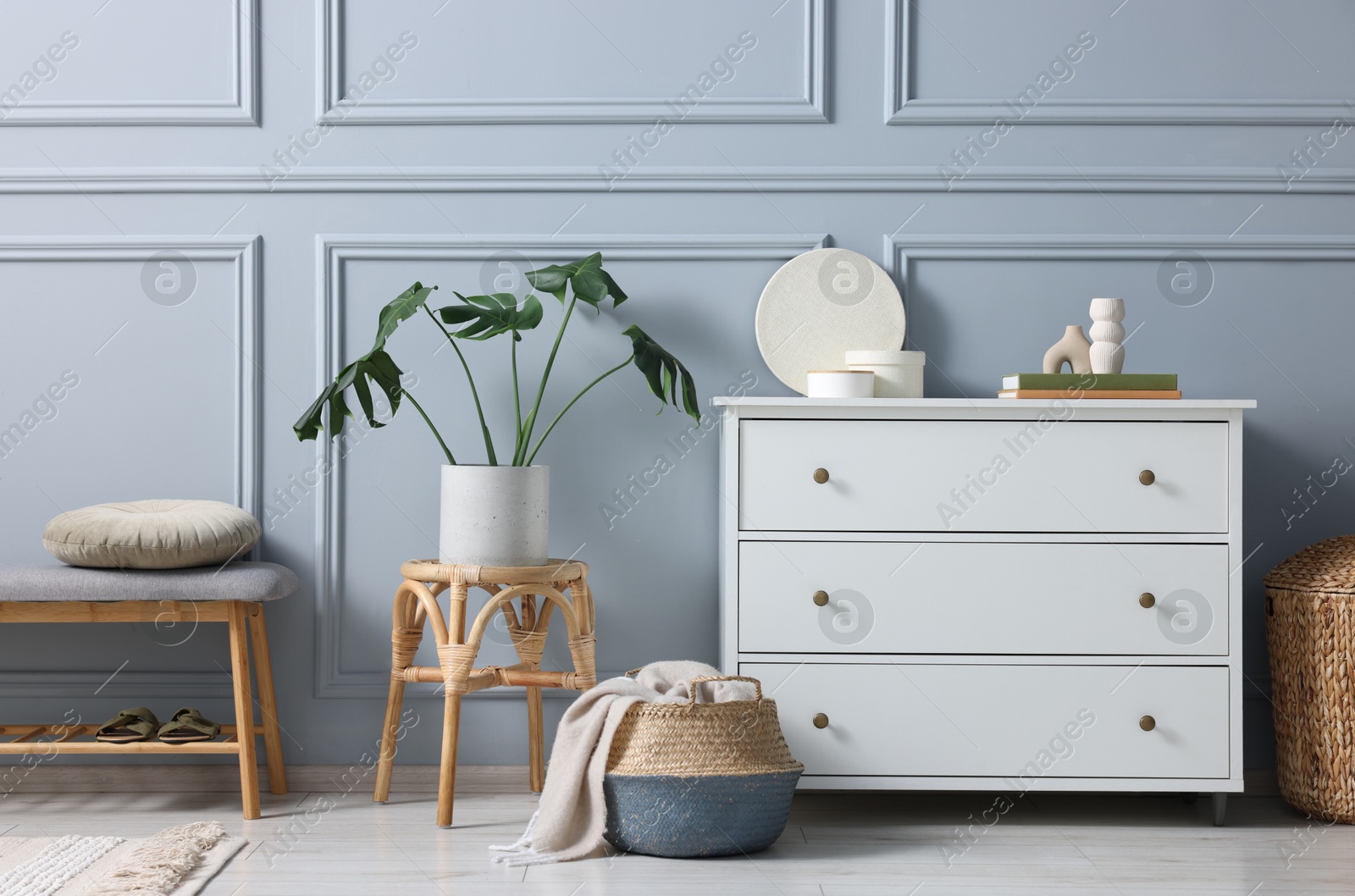 Photo of Stylish interior with stool and chest of drawers near light grey wall