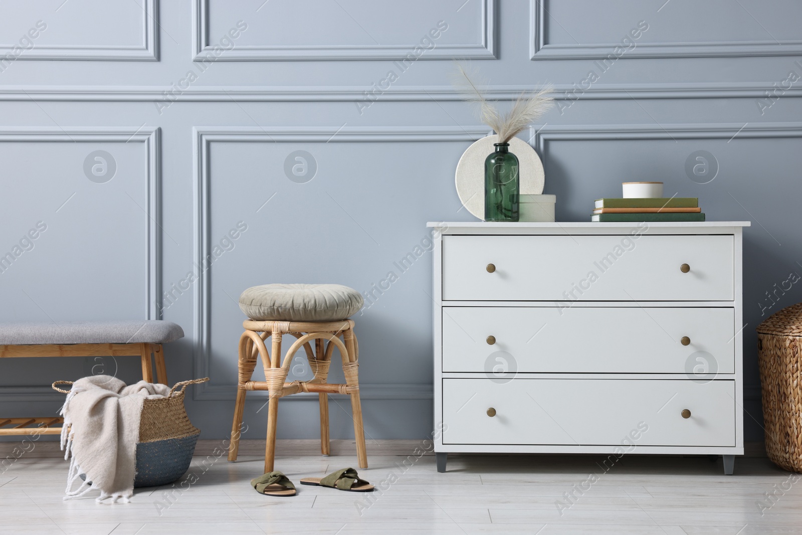 Photo of Stylish interior with stool and chest of drawers near light grey wall