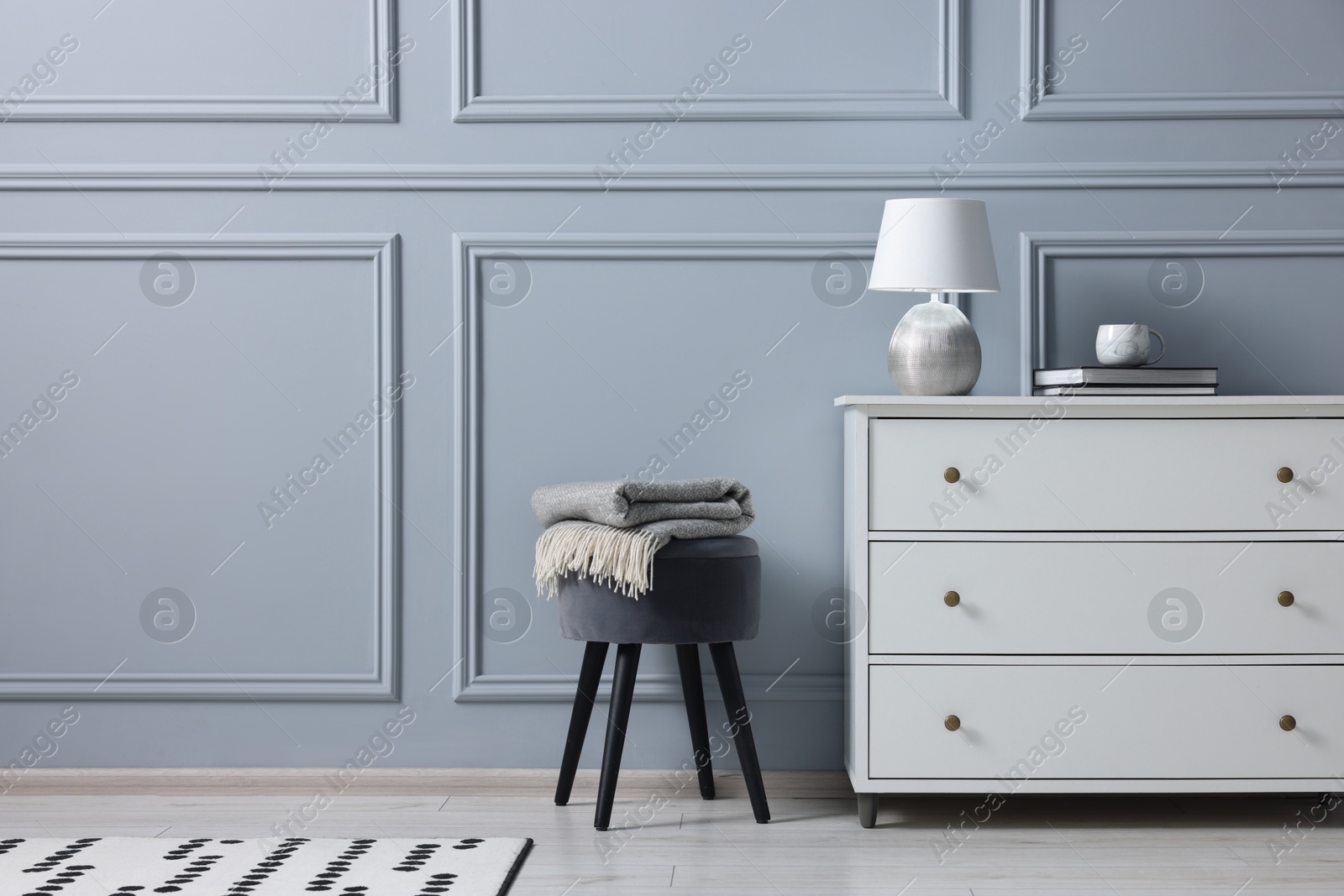 Photo of Stylish interior with stool and chest of drawers near light grey wall, space for text