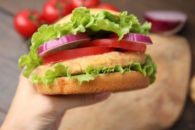 Woman holding vegetarian burger with chickpea cutlet at table, closeup