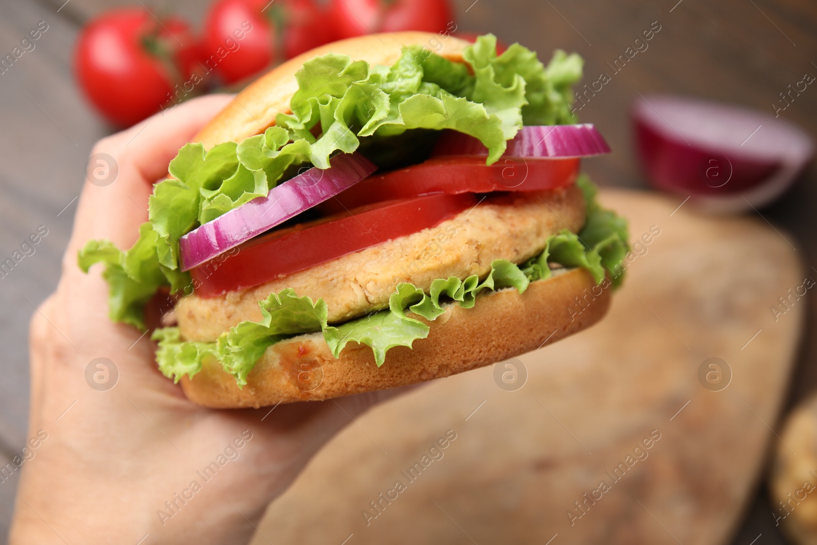 Photo of Woman holding vegetarian burger with chickpea cutlet at table, closeup