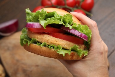 Photo of Woman holding vegetarian burger with chickpea cutlet at table, closeup