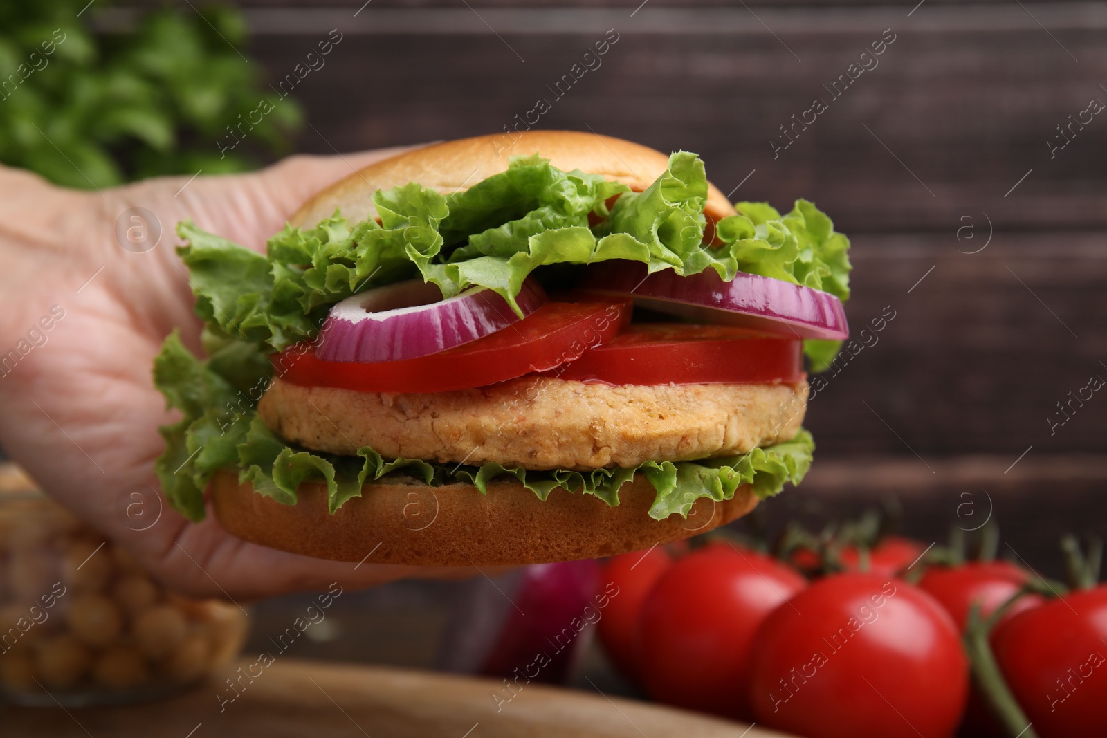 Photo of Woman holding vegetarian burger with chickpea cutlet at table, closeup