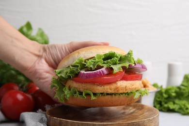 Photo of Woman holding vegetarian burger with chickpea cutlet at table, closeup