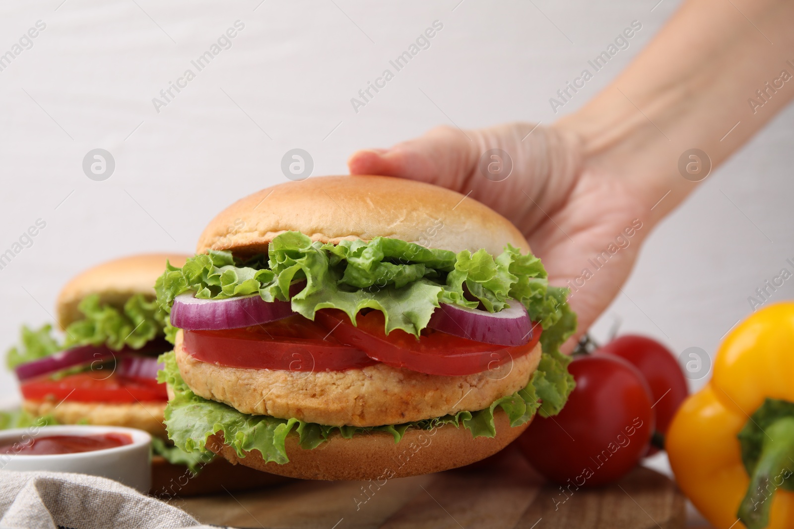 Photo of Woman holding vegetarian burger with chickpea cutlet at table, closeup