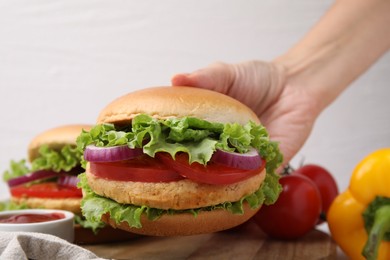 Woman holding vegetarian burger with chickpea cutlet at table, closeup