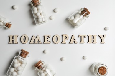 Photo of Word Homeopathy and pills on white background, flat lay