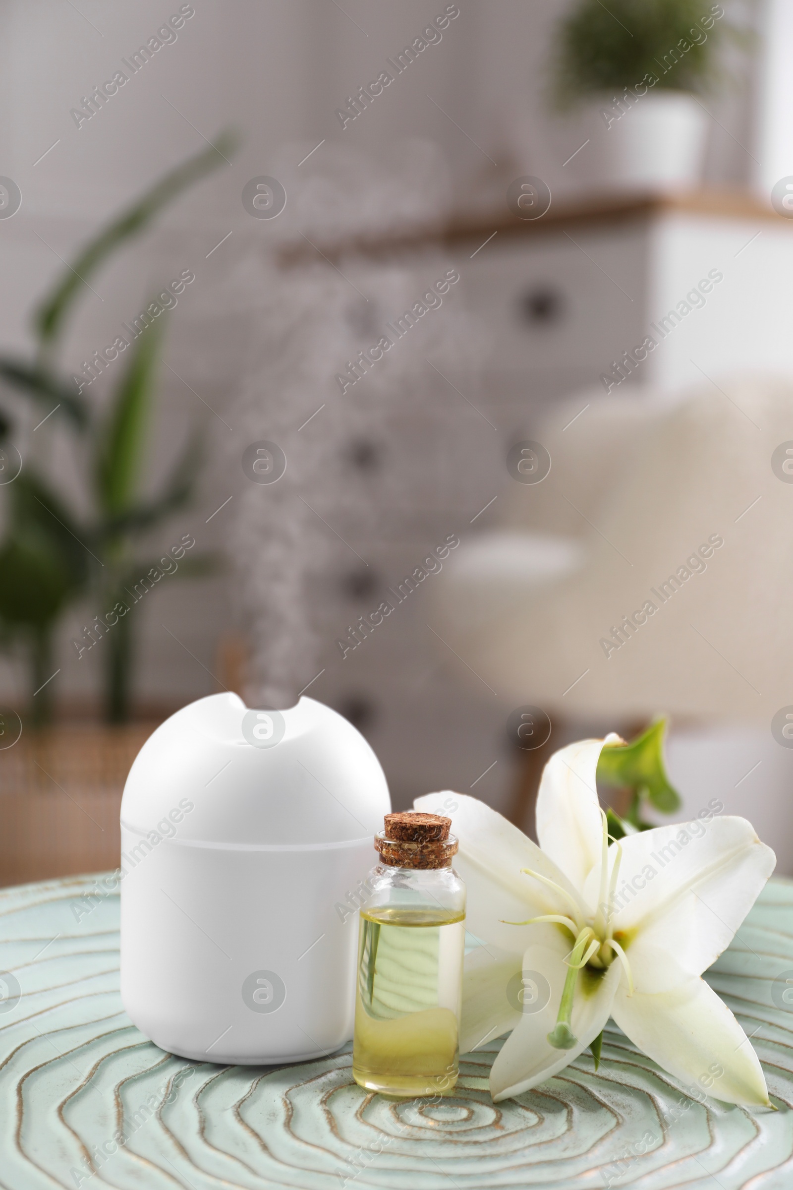 Photo of Essential oil diffuser, cosmetic product and lily flower on table at home