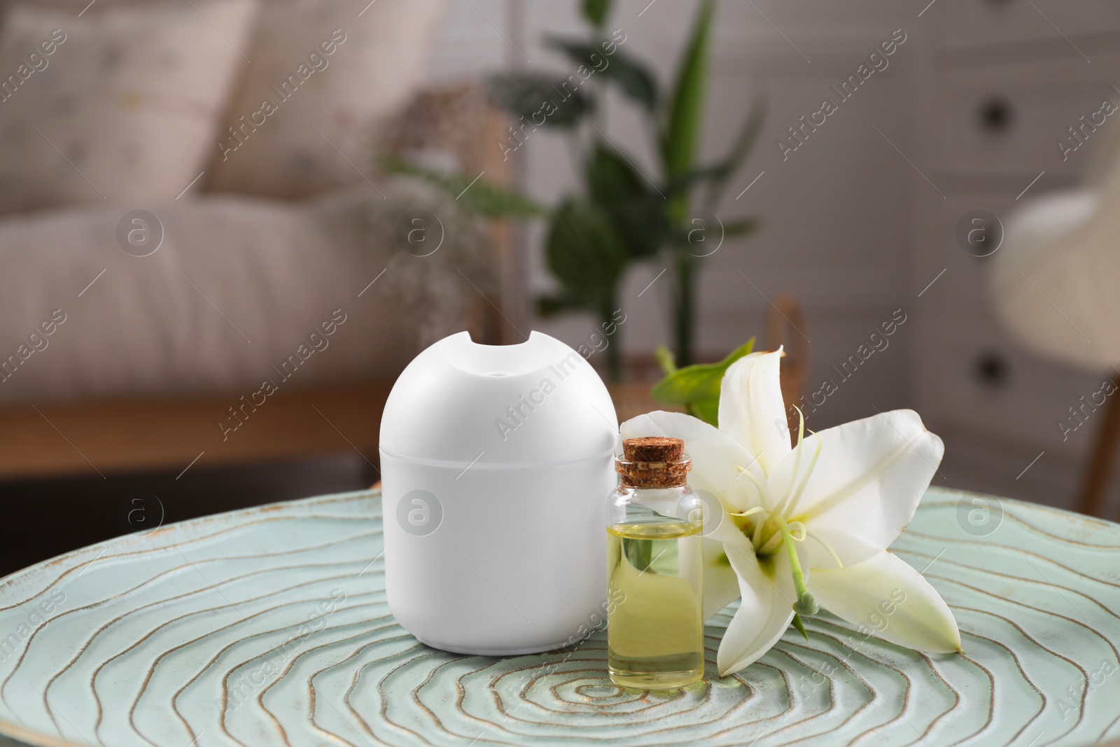 Photo of Essential oil diffuser, cosmetic product and lily flower on table at home