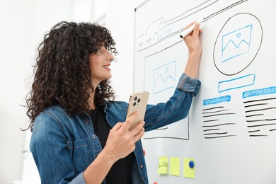 Developing UI design. Woman drawing website wireframe on whiteboard indoors