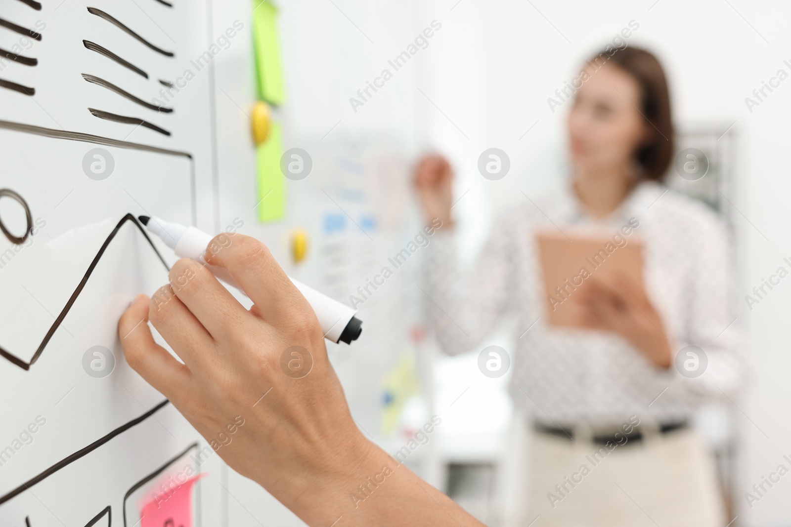 Photo of Developing UI design. Man and woman drawing website wireframe on whiteboard indoors, selective focus