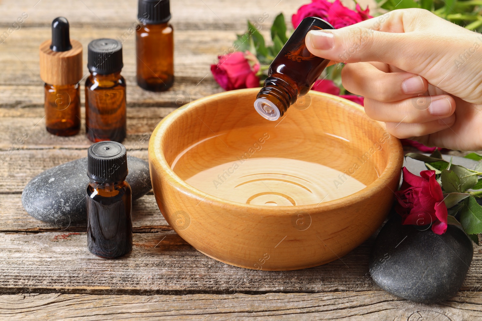 Photo of Woman dripping essential oil into bowl with water at wooden table, closeup