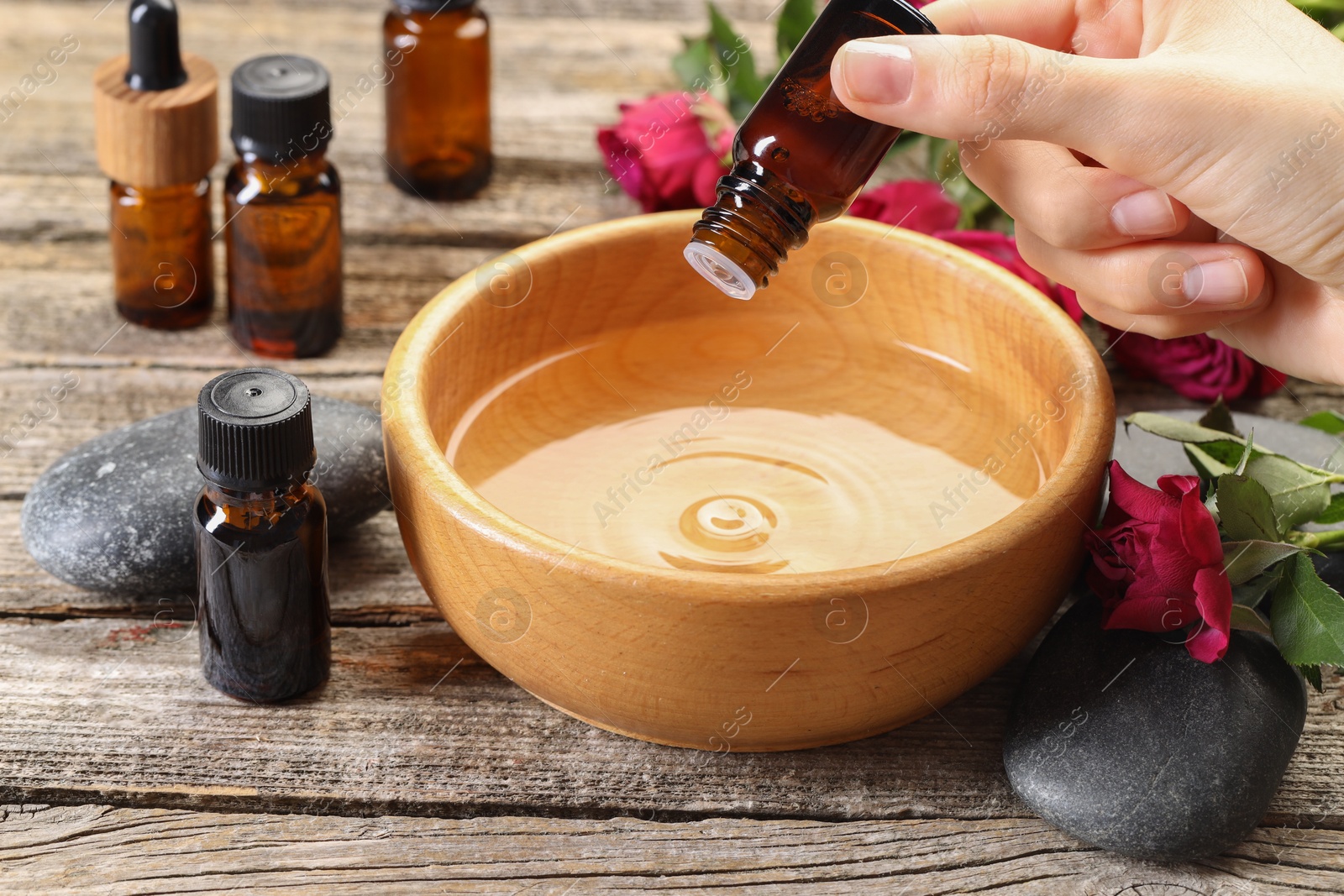 Photo of Woman dripping essential oil into bowl with water at wooden table, closeup