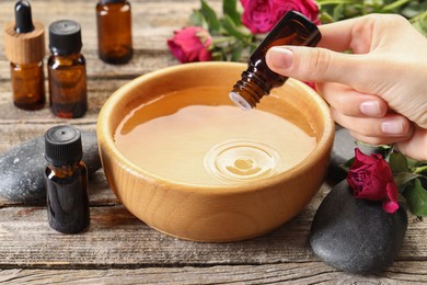 Photo of Woman dripping essential oil into bowl with water at wooden table, closeup