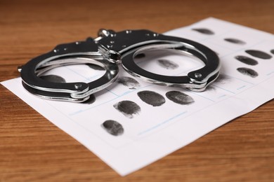 Paper sheet with human fingerprints and handcuffs on table, closeup. Criminal conviction